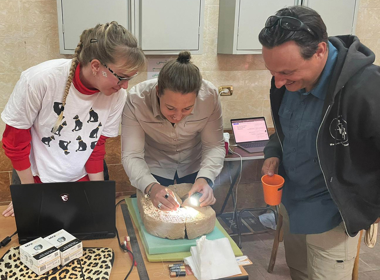 Three people working over an Egyptian artifact