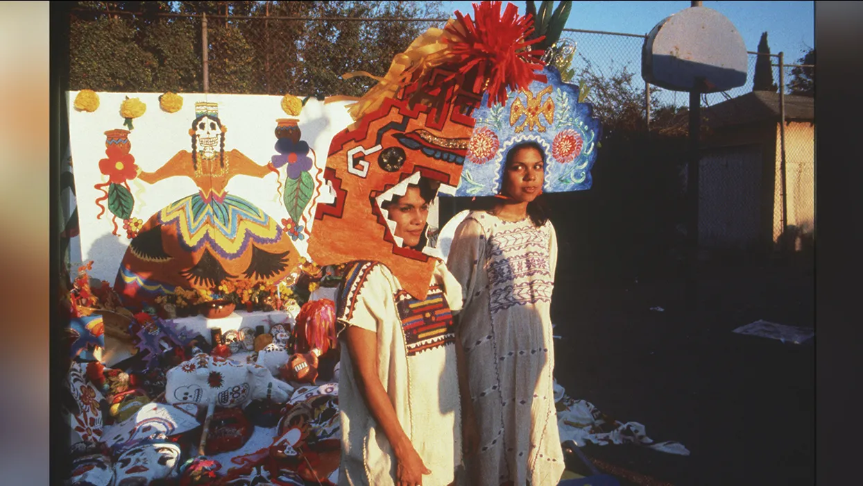 : Photograph of Ofelia Esparza and her daughter, Rosanna Esparza-Ahrens, wearing paper mache constructions worn as helmets with large geometric designs, 1980.