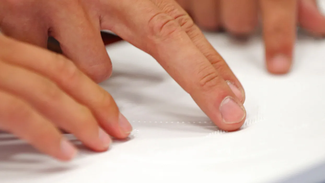 Fingers trace Braille on a page.