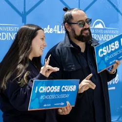 Two people holding up “Choose CSUSB Day” signs at a photo booth during the 2024 event