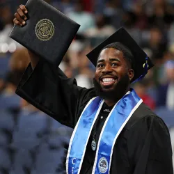 Student smiles and holds up diploma at commencement